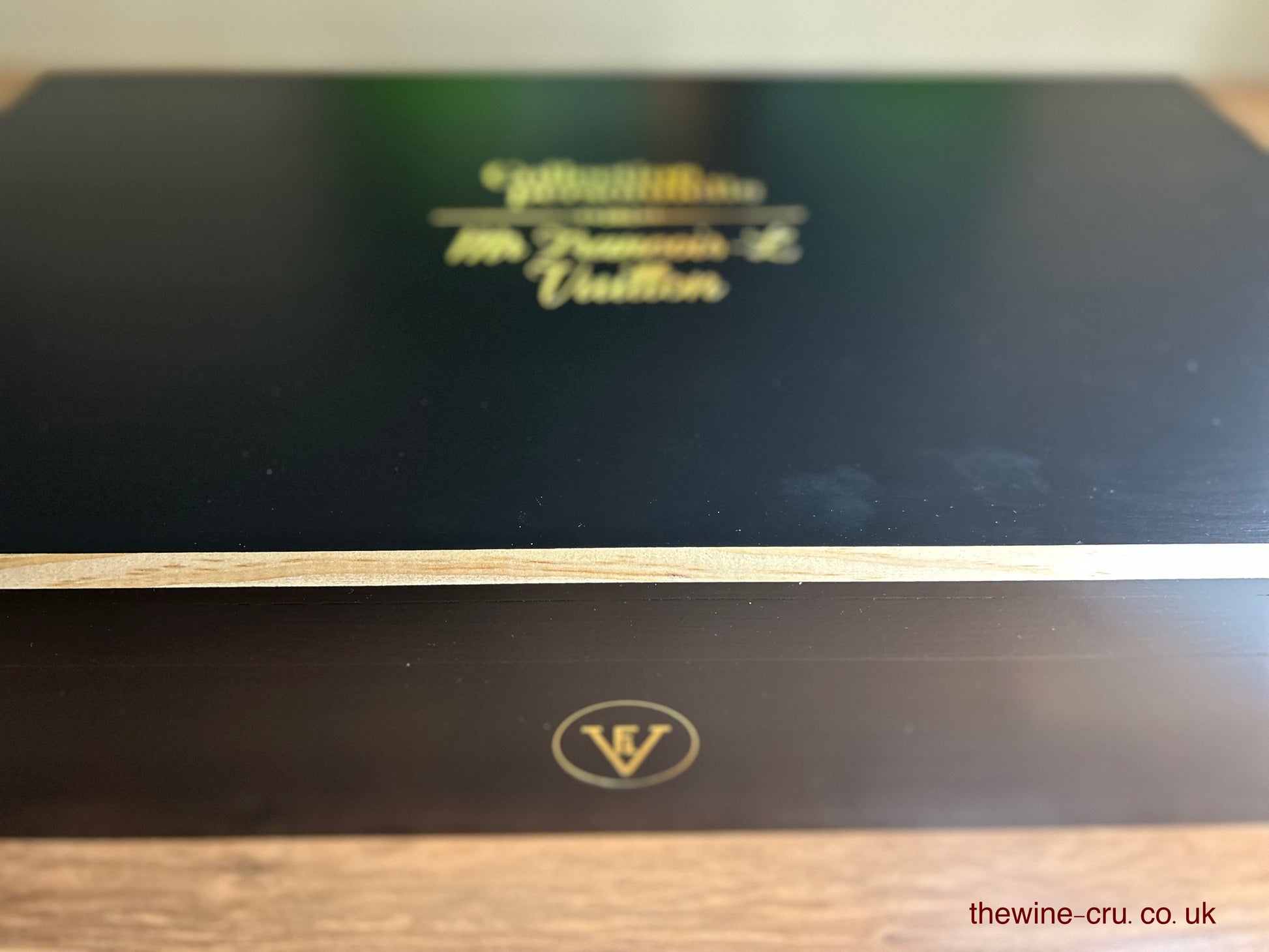 Close-up of a black wine box with gold text and logo on a wooden surface.