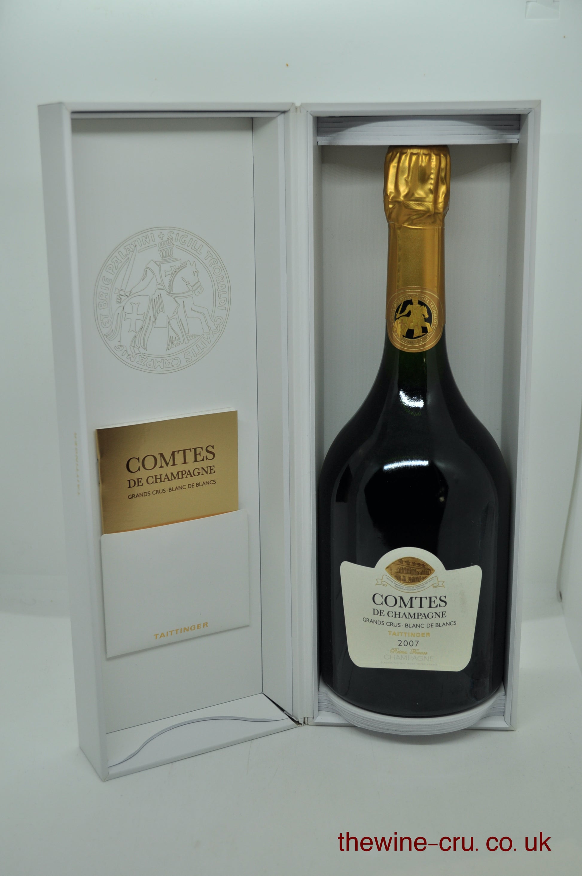 A bottle of Comtes de Champagne champagne presented inside an open white gift box, with the bottle showing a dark glass body, cream label, and gold foil neck.